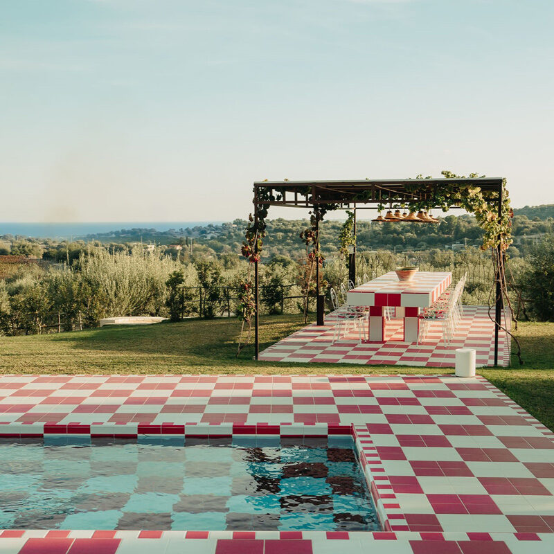 A long dining table under a vine-covered pergola beside the checkered pool